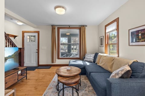 Welcoming living room with L-shaped sectional, large smart TV, and front entry — original staircase with classic wood banister adds timeless Minneapolis character.