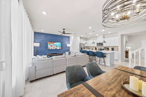 Enjoy a beautifully designed living space with a striking blue accent wall that adds an airy feel. Relax on plush gray sofas and gather around the modern dining table under a stylish chandelier for delightful moments.