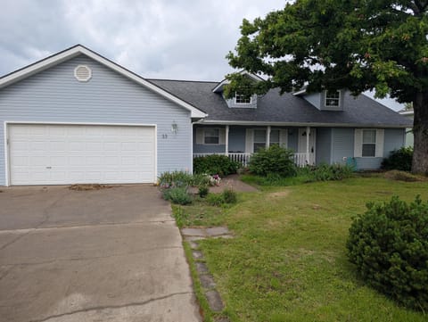 Light blue siding covers the single-story house with a two-car garage, white trim, and a large tree shading the front lawn.