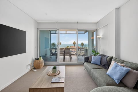 Soft seating and a calm palette create a welcoming space to relax, with doors opening wide to the balcony and sea beyond.