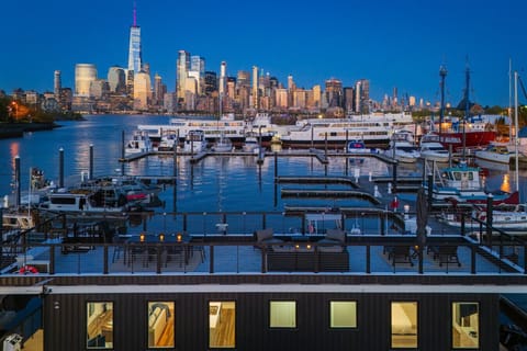 Rooftop deck at blue hour, Liberty Landing Marina. One World Trade and the full Manhattan skyline directly across the Hudson