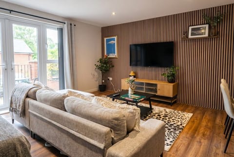 Sunlit open plan lounge with French doors to the terrace and a statement oak slat smart TV wall.