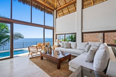 Floor-to-ceiling glass floods this soaring living room with ocean views and tropical light, opening to the private pool terrace of this Puerto Vallarta, palapa villa