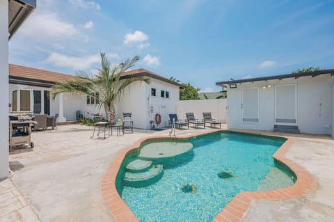 Bright pool area with unique curved edges, surrounding lounge chairs, and clean white walls reflecting the island sun