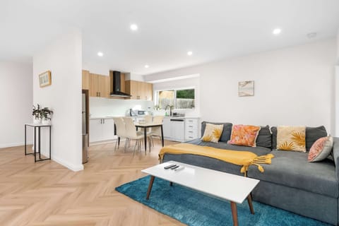 **`image_efc013.png`**
Relax in this spacious, open-plan living and dining area featuring herringbone wood flooring, a deep grey sectional sofa styled with colorful throw pillows, a vibrant teal rug, a white coffee table, and a seamless flow into a m