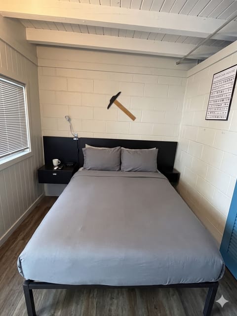 Queen bed beneath a vintage hammer and `American House` architectural chart — The Architect`s Suite signature