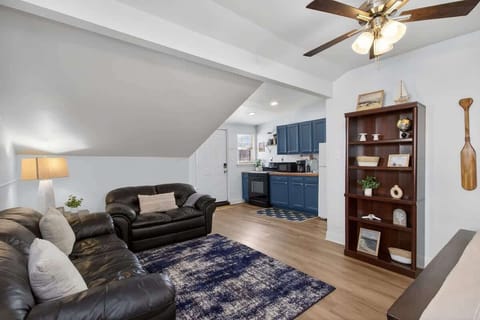 Open-concept living area with black leather seating, a cozy rug, and a seamless flow into the fully equipped kitchen with blue cabinetry—ideal for relaxing and entertaining.