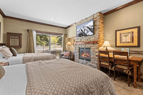 Unwind in your cozy mountain retreat with two plush beds, a stone fireplace, and a workspace overlooking serene forest views—your perfect alpine escape.