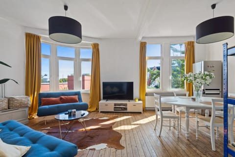 Bright and spacious living area with large windows that fill the room with natural light. Relax on comfortable sofas, enjoy the open seating layout, and gather around the dining table while overlooking neighborhood views.