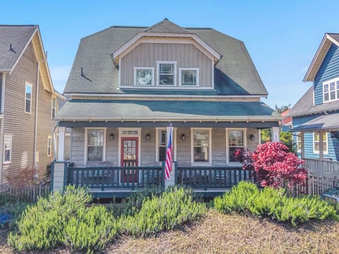 Charming coastal cottage with wraparound porch and manicured gardens in a picturesque neighborhood setting.