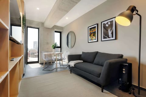 Bright living room with a cozy sofa, smart TV, and natural light from floor-to-ceiling windows.