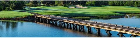 The golf course features manicured fairways, strategic sand traps, and a scenic wooden bridge crossing a tranquil water hazard—a beautiful backdrop for the property.