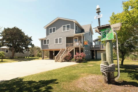 A welcoming coastal retreat with elevated charm, set amid lush greenery and mature trees, featuring ample parking and a distinctive lighthouse marker at the entrance.