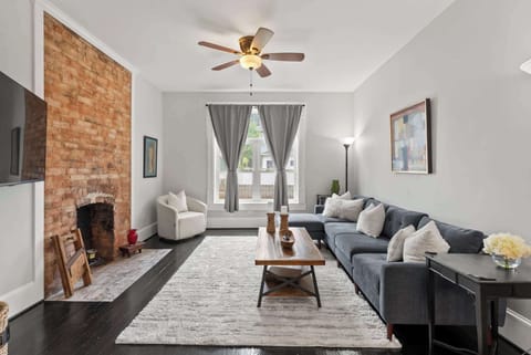 Curl up by the exposed brick fireplace in a bright living room w/ tall windows & ceiling fan.