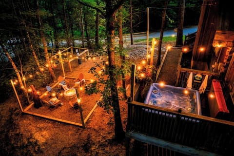 Stunning aerial view of Cubby Bear Den at night featuring private hot tub, wraparound deck, and string lights nestled in the Smoky Mountains