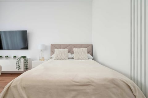A minimalist bedroom area with a neatly made bed, soft neutral bedding, and vertical wall paneling creating a calm atmosphere.