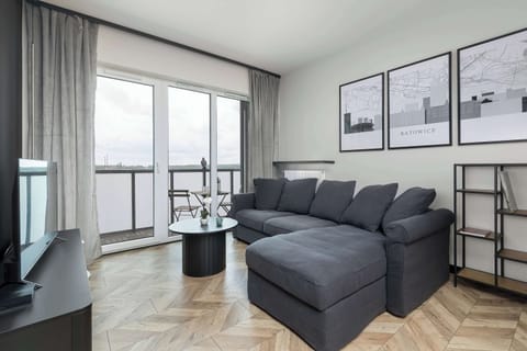 A modern living room with a large gray sectional sofa, floor-to-ceiling curtains, and access to a balcony.