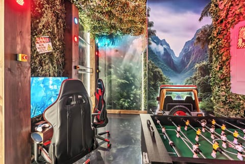Experience an exciting gaming lounge featuring vibrant mountain murals, plush gaming chairs, and a foosball table for friendly competition, all illuminated by soft ambient lighting that enhances the lively atmosphere.