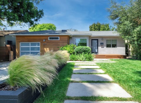 Out front, the home presents a clean, modern curb appeal with a manicured lawn, stepping stone pathway, and a mix of wood and stucco finishes that create a warm, balanced exterior. Mature landscaping frames the approach, giving a sense of privacy while maintaining an inviting arrival.