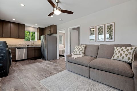 Bright, open living and kitchen area with comfortable sofa, ceiling fan, and full kitchen