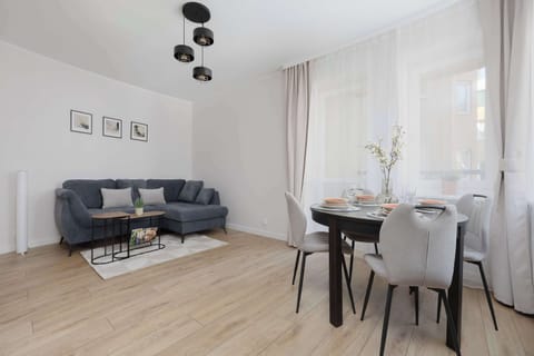 A bright living room connected to the dining area, featuring a gray corner sofa and a table with modern chairs by the window.