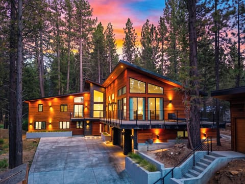 Twilight mountain retreat with dramatic windows, warm exterior lighting, and a peaceful pine forest setting.