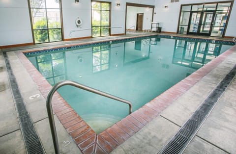 Tiled indoor pool with steps into the water and large windows overlooking garden greenery.