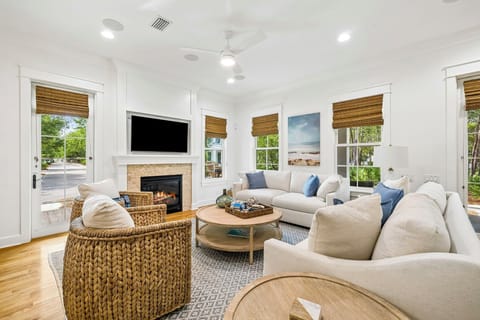 Sink into plush seating around the fireplace, where warm wood tones and coastal artwork create your perfect gathering space. Natural light floods through multiple windows, inviting peaceful moments of relaxation.