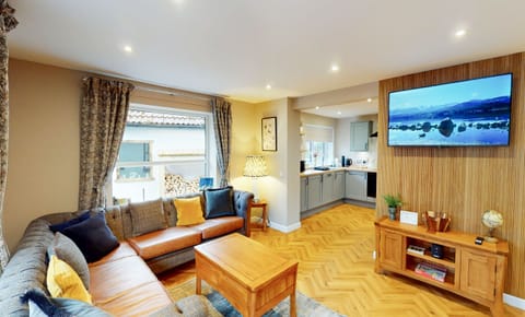 Relax and unwind in the bright and spacious open-plan lounge at Kestrel Lodge. This inviting living area features a generous corner sofa, wooden coffee table, and beautiful herringbone parquet flooring. The cosy yet stylish space flows seamlessly into the kitchen, making it perfect for family time together after a day exploring the Cairngorms.