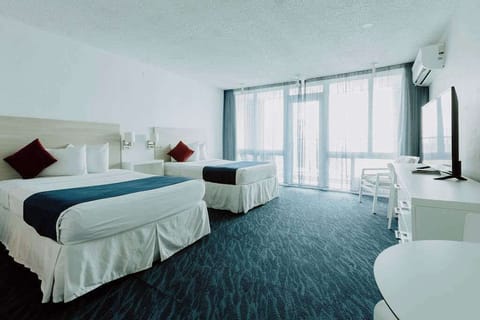 Bright Isla Verde studio layout showing beds, TV, dining table, and balcony doors with natural light.