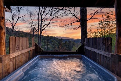 Bubbling hot tub overlooking rolling forested hills under a vibrant sunset sky. (Isaiah's Cabin)