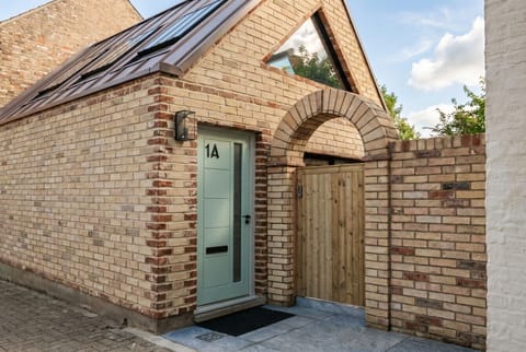 A striking architect-designed mews cottage with a copper roof and arched brick entrance.