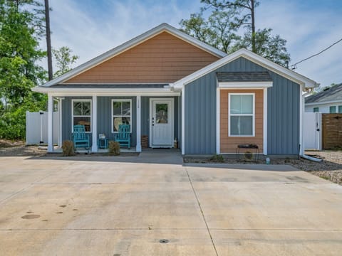 Front exterior with blue-gray siding, brown upper section, teal chairs, white door, and concrete driveway