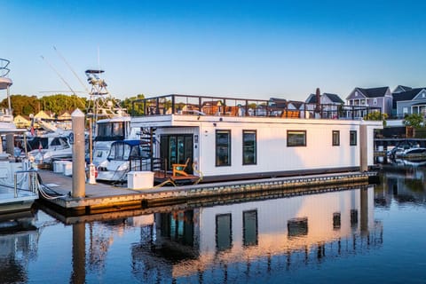 Selah Sailor in full morning light at Barefoot Marina, with the rooftop deck, open waterway, and the property`s reflection stretching across the still water below.