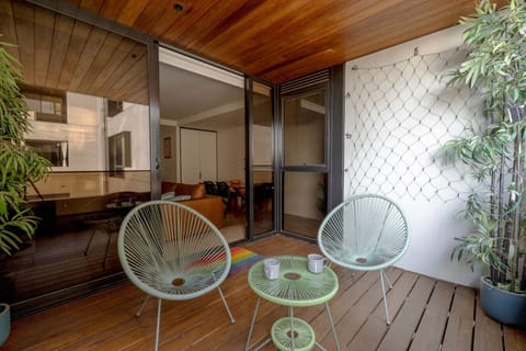 Sip your morning coffee or enjoy an evening drink on this private, wood-paneled balcony, featuring comfortable retro-style chairs nestled among lush greenery.