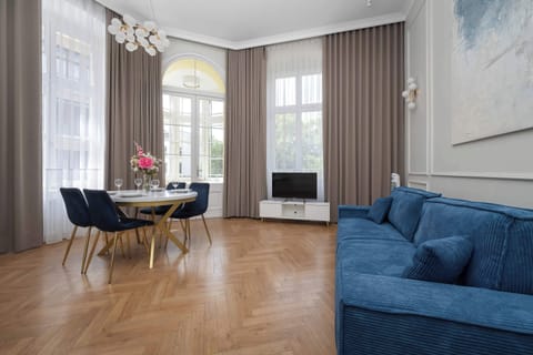 A stylish living room with a blue sofa, elegant curtains, and a dining table placed near tall windows.