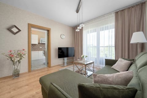 A cozy bedroom with a large green sectional sofa and coffee table. Bright natural light enters through the balcony doors, creating a warm and inviting atmosphere.