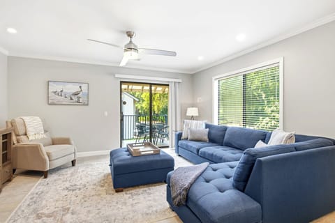 Deep navy upholstery and tufted textures anchor this airy living room, where natural light streams through wide windows. Morning rays illuminate the patterned rug, creating a serene corner for slow coffee and quiet conversation.