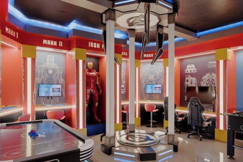Experience a vibrant entertainment room inspired by your favorite superhero universe, featuring bold red and blue accents, a sleek gaming setup, and an arcade table, all enhanced by dynamic LED lighting for endless enjoyment.