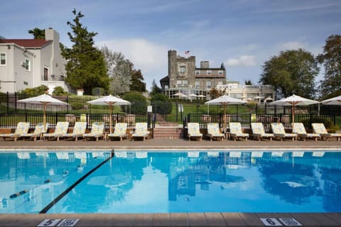 Poolside loungers and umbrellas facing a stone manor across the water.