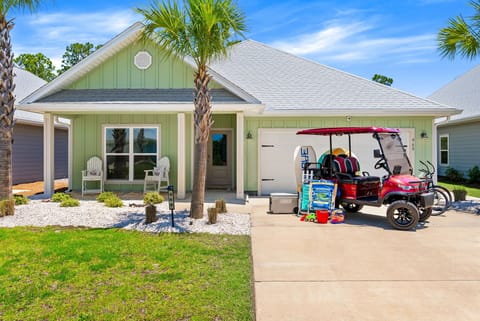 A charming coastal-style home with refreshing green siding, palm trees, and a welcoming front porch—your home base for a beach getaway. A golf cart awaits in the driveway for easy neighborhood cruising.