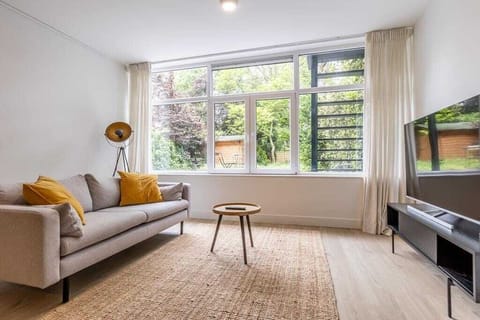 The apartment features a spacious open-plan living and dining area with large windows facing greenery, creating a bright and calm interior. The modern kitchen is fully equipped and integrated into the living space.