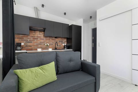 Bright modern living room with a gray sofa, white walls, and a stylish exposed brick kitchen in the background.