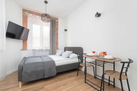 A stylish studio room featuring a comfortable bed, a dining corner, and minimalist décor. Large windows make the apartment feel airy and inviting.