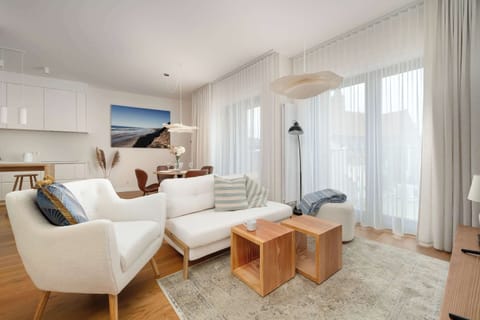 A bright living room with a comfortable sofa, wooden coffee table, and large windows letting in plenty of natural light. Soft neutral tones create a calm and inviting atmosphere.