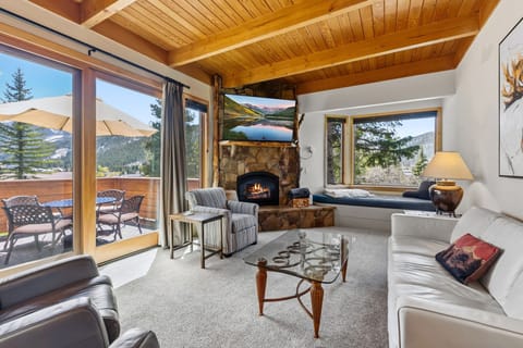 Unwind in your bright, airy living space featuring vaulted wood-beam ceilings, a cozy stone fireplace, and floor-to-ceiling windows framing breathtaking mountain views. Step outside to your private deck and soak in the alpine serenity.