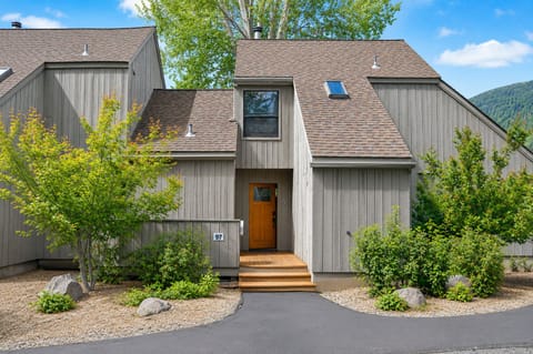 Modern mountain retreat with natural wood siding and welcoming entrance, nestled among lush greenery with scenic hillside backdrop.