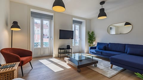 Relax in the bright and airy living room with a stylish blue sofa, natural light streaming through large windows, and a cozy reading corner for ultimate comfort. #LisbonStay #CityApartment #AirbnbLisbon #HomeAwayFromHome #LovelyStay