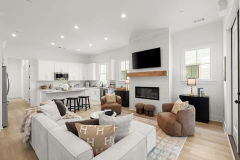 Bright open-concept living room with fireplace, TV, and spacious kitchen