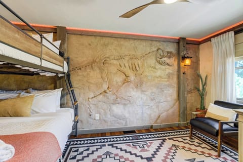 A full dinosaur skeleton spans the entire fossil wall behind the bunk bed, with real bones set directly into the plaster and lit from above. There is nothing else like this room in Colorado Springs.